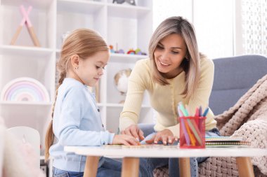 Anne, kızına beyaz masada alfabe öğretiyor.