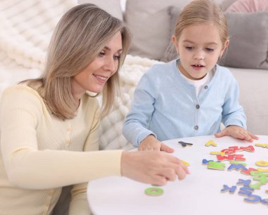 Anne, kızına beyaz masada alfabe öğretiyor.
