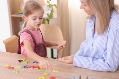 Konuşma terapisti kız alfabeyi öğretiyor. İçerideki ahşap masada harflerle.