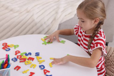 Beyaz masada harflerle alfabe öğrenen küçük bir kız.