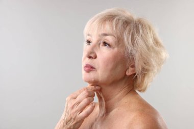 Üst düzey kadın açık gri arka planda boynuna dokunuyor. Metin için boşluk