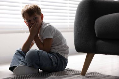 Çocuk tehlikede. Evdeki koltuğun yanında korkmuş küçük çocuk.