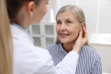 Doktor klinikte hastanın kulağına işitme cihazı takıyor.