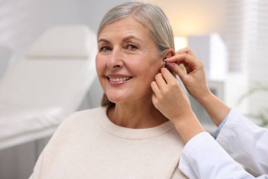 Doktor klinikte hastanın kulağına işitme cihazı takıyor.