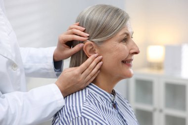 Doktor klinikte hastanın kulağına işitme cihazı takıyor.