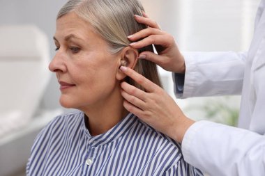 Doktor klinikte hastanın kulağına işitme cihazı takıyor.