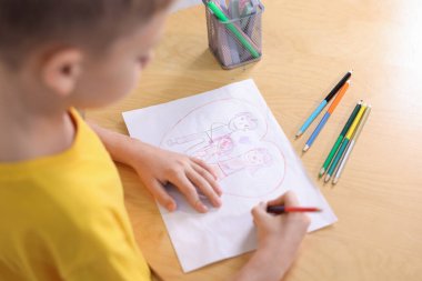 Ahşap masada aile çizen şirin küçük çocuk, yakın plan.