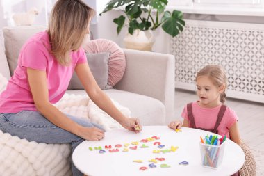 Anne, kızına beyaz masada alfabe öğretiyor.