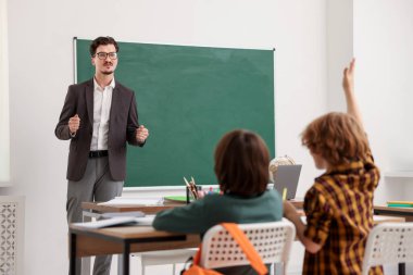 Çocuk sınıfta öğretmeninin sorusuna cevap vermek için elini kaldırıyor.