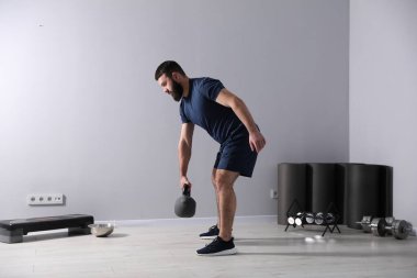 Spor salonunda kettlebell ile egzersiz yapan güçlü bir adam.