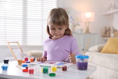 Beyaz masa içinde fırça çizen küçük kız.