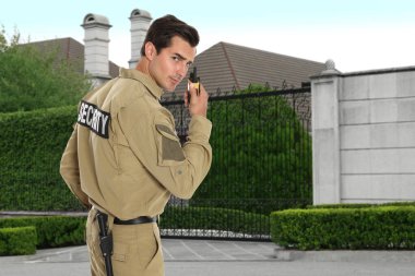 Üniformalı güvenlik görevlisi evin yakınında telsiz kullanıyor. Özel mülk koruması