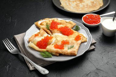 Kırmızı havyarlı leziz krepler ve siyah desenli masaya ekşi krema, yakın plan.