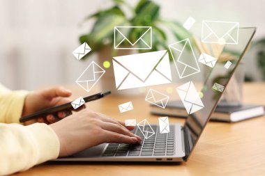 E- posta bildirimi. Masada dizüstü bilgisayar ve cep telefonu kullanan bir kadın, yakın plan. Ekranda uçuşan harfler