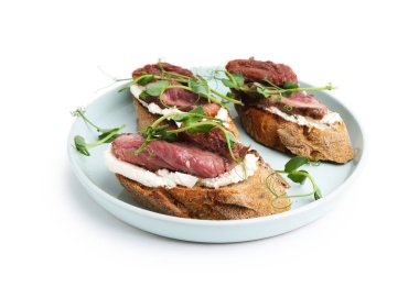 Biftek, krem peynir, güneşte kurutulmuş domates ve beyaz üzerine izole edilmiş mikro yeşillikler ile nefis bruschetalar.