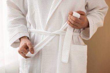 Bornozun kemerini bağlayan adam içeride, yakın plan.