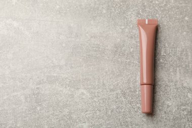 Gri desenli arka planda güzel çıplak dudak parlatıcısı, üst manzara. Metin için boşluk