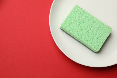 Kırmızı arka planda mutfak süngeri ve plaka, üst manzara. Metin için boşluk