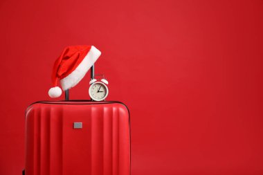 Noel tatili. Kırmızı zemin üzerinde Noel Baba şapkası ve alarm saati olan bavul, metin için boşluk