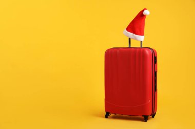 Noel tatili. Turuncu arka planda Noel Baba şapkalı kırmızı bavul, mesaj için boşluk