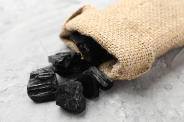 Çuval içinde siyah kömür parçaları gri desenli masada, yakın plan.