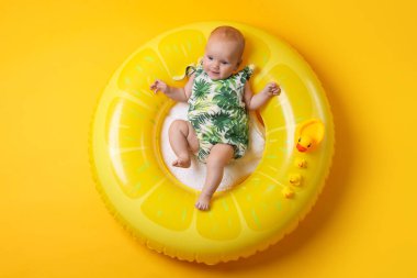 Oyuncak ördekleri olan, turuncu arka planda şişme halka takan şirin bir bebek.