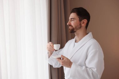 İçeride pencerenin yanında bir fincan kahveli bornoz giyen bir adam. Metin için boşluk