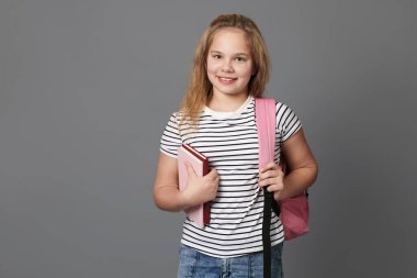 Gri arka planda kitapları ve sırt çantası olan tatlı bir kız.