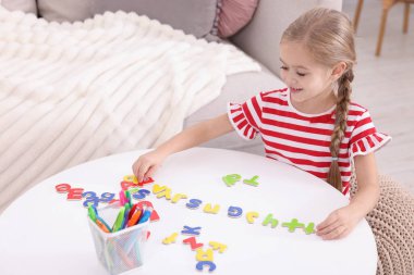 Beyaz masada harflerle alfabe öğrenen küçük bir kız.