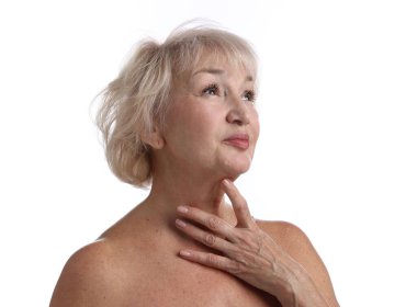 Yaşlı kadın beyaz arka planda boynuna dokunuyor.