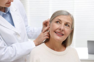 Doktor klinikte hastanın kulağına işitme cihazı takıyor.