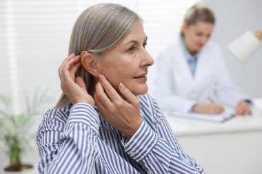 İşitme cihazı olan yaşlı bir kadının klinikte doktorla randevusu var.