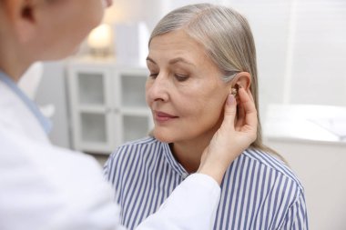 Doktor klinikte hastanın kulağına işitme cihazı takıyor.