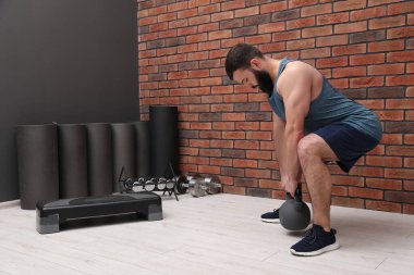 Spor salonundaki tuğla duvarın yanında kettlebell ile egzersiz yapan adam.