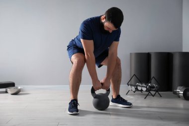 Spor salonunda kettlebell ile egzersiz yapan güçlü bir adam.