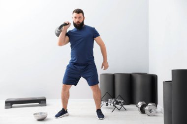 Spor salonunda kettlebell ile egzersiz yapan güçlü bir adam.