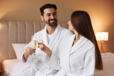 Yataklarında köpüklü şarap bardakları olan bornozlu mutlu bir çift.