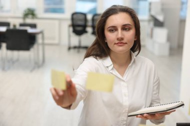 Ofiste elinde kalem ve defter tutan bir kadın var.