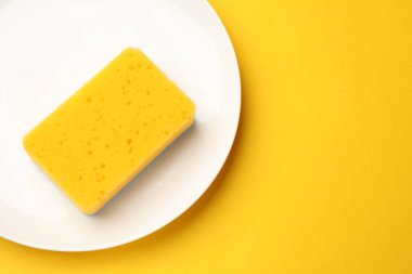 Temiz mutfak süngeri ve sarı arka planda plaka, üst manzara. Metin için boşluk