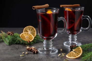 Cam bardaklarda lezzetli şarap, baharatlar ve gri masada köknar dalları, yakın plan.