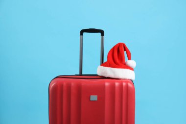 Kırmızı bavulda açık mavi arka planda Noel Baba şapkası. Noel tatili