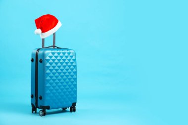 Noel tatili. Açık mavi arka planda kırmızı Noel Baba şapkalı bavul. Metin için boşluk