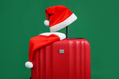 Noel tatili. Yeşil arka planda Noel Baba şapkası olan kırmızı bavul.