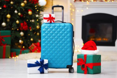 Christmas vacation. Suitcase with Santa hat and gift boxes indoors