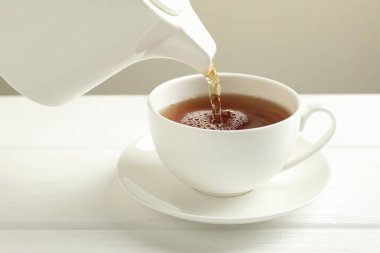 Beyaz ahşap masada çaydanlıktan fincana sıcak çay dökülüyor, yakın plan.