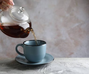 Gri masada çaydanlıktan fincana sıcak çay dolduran kadın, yakın plan. Metin için boşluk