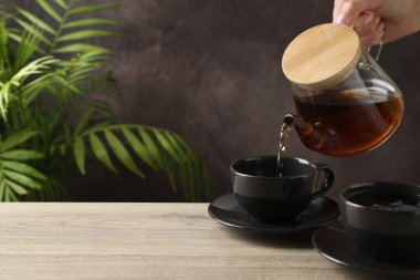 Ahşap masada çaydanlıktan fincanlara sıcak çay dolduran kadın, yakın plan. Metin için boşluk