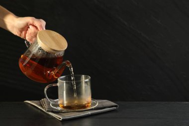 Siyah ahşap masada çaydanlıktan fincana sıcak çay dolduran kadın, yakın plan. Metin için boşluk
