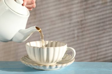 Açık mavi ahşap masada çaydanlıktan fincana sıcak çay dolduran kadın, yakın plan. Metin için boşluk