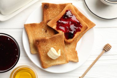 Beyaz ahşap masada tereyağı, bal, reçel ve çay ile servis edilen taze kızarmış ekmek dilimleri.